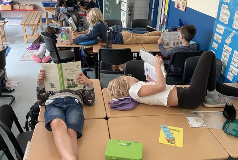 Kinder lesen auf den Schultischen liegend in Büchern